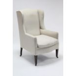A late 19th century wing-back armchair, upholstered off-white material & on short square tapered