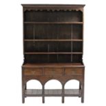 AN 18th century OAK DRESSER, fitted three shelves above three frieze drawers with shaped brass swing