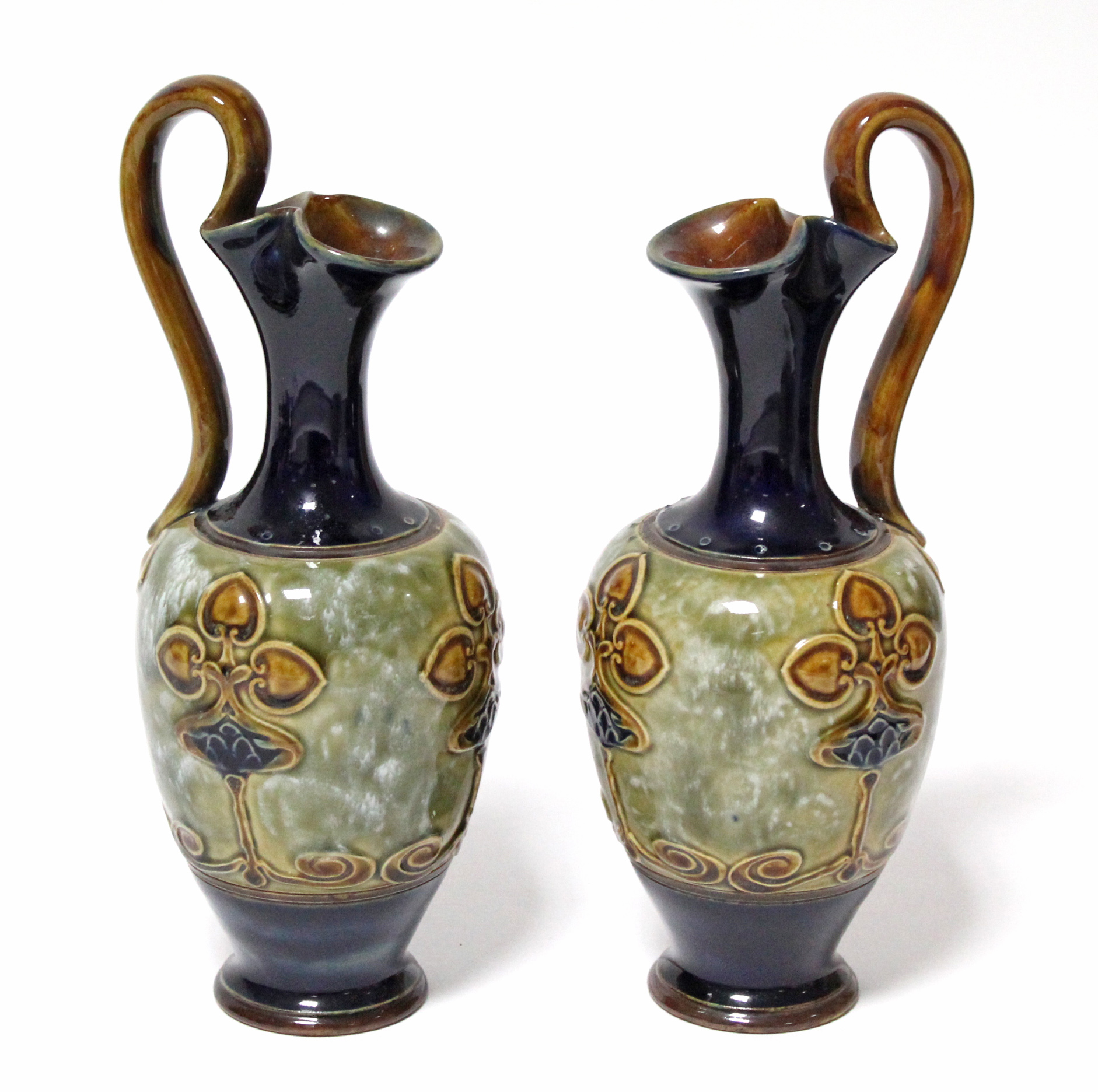 A pair of Royal Doulton stoneware ewers with art nouveau stylised floral motifs; 9½” high.