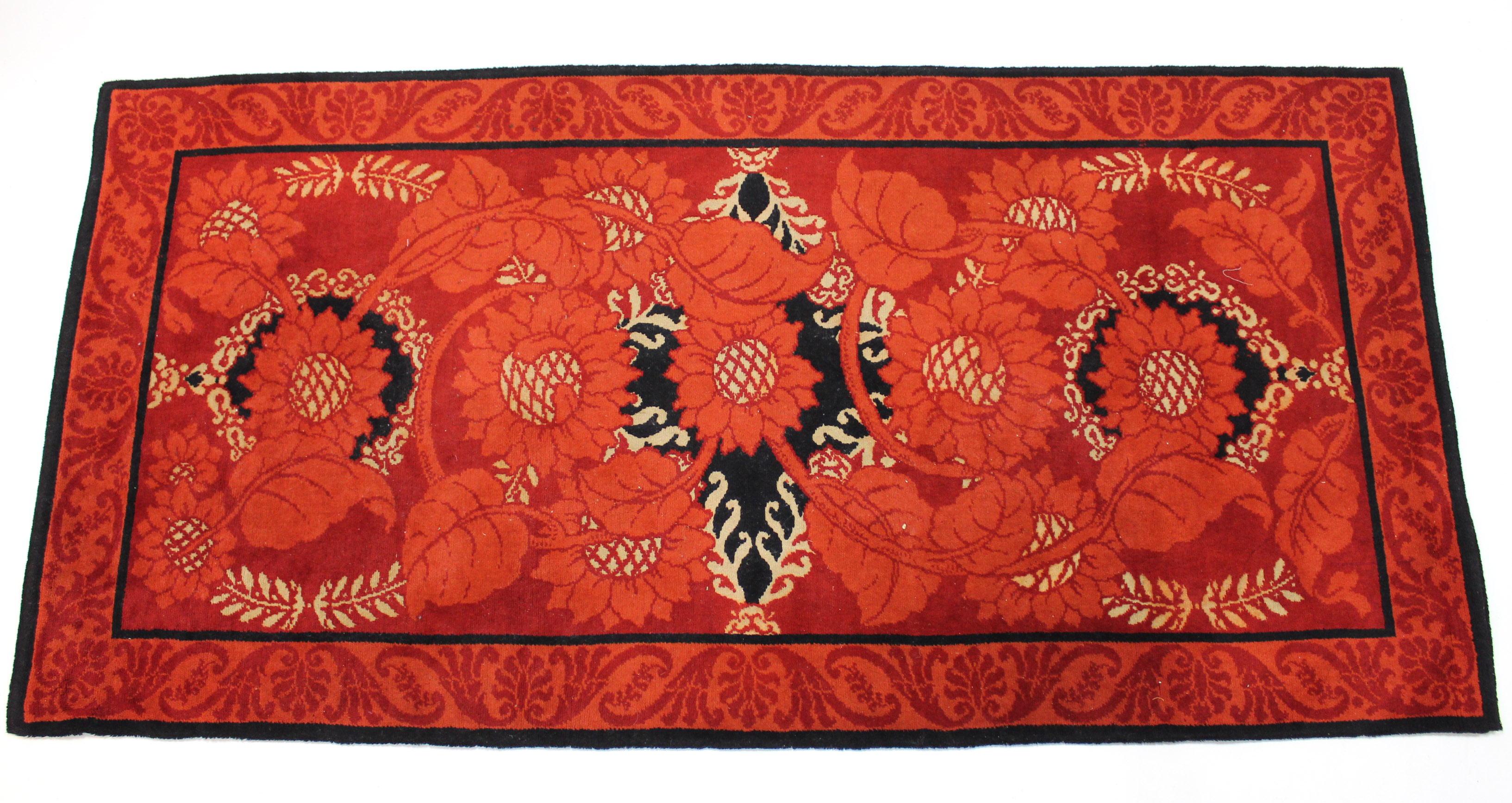 An early 20th century Arts & Crafts style rug of crimson ground, with stylised floral motifs; 6’