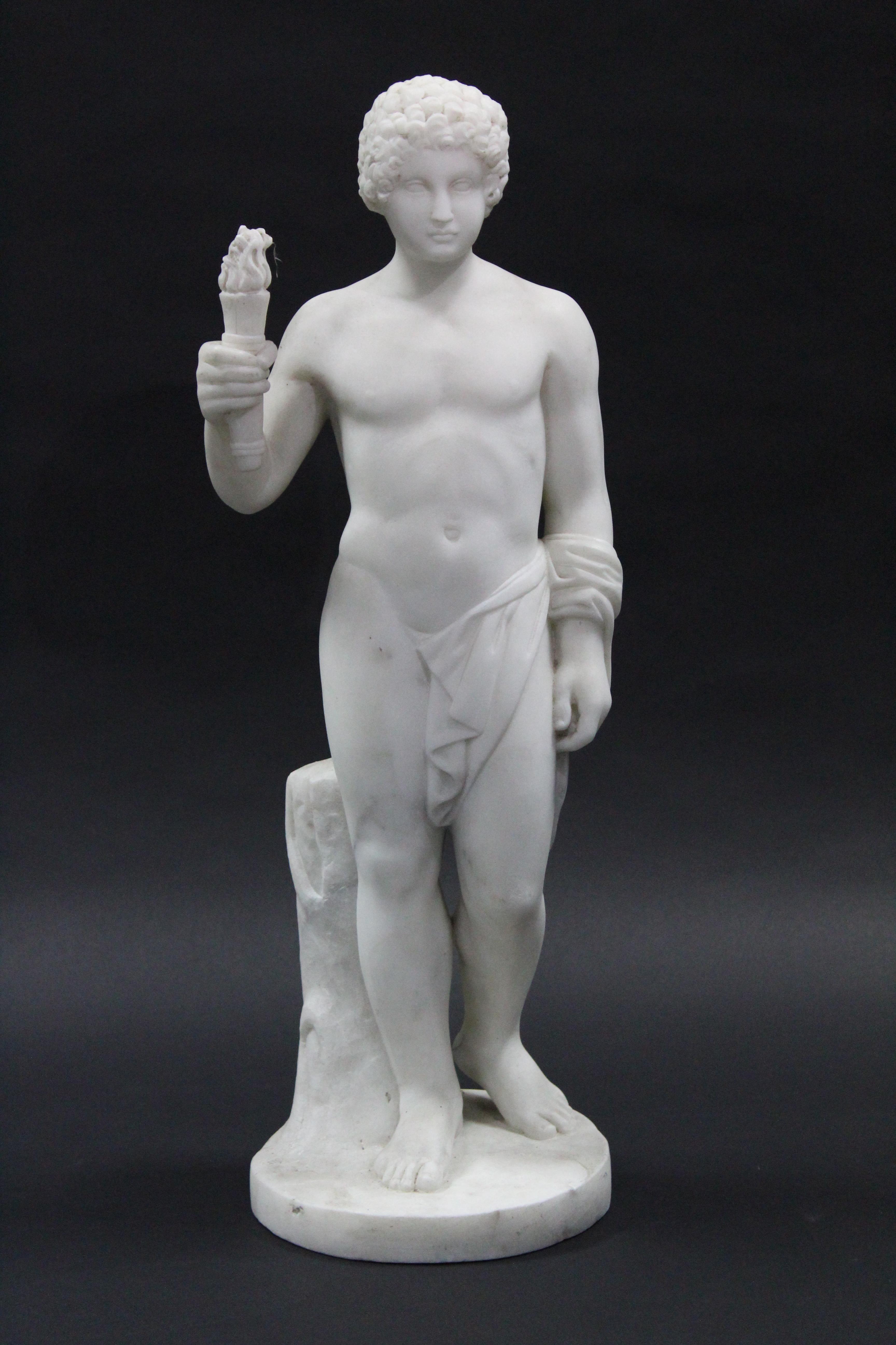 A sculptured white marble standing semi-nude figure of a young man holding a flaming torch in his