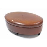 A Crate & Barrel tan leather oval pouffe/stool on ebonised feet, 48” wide.