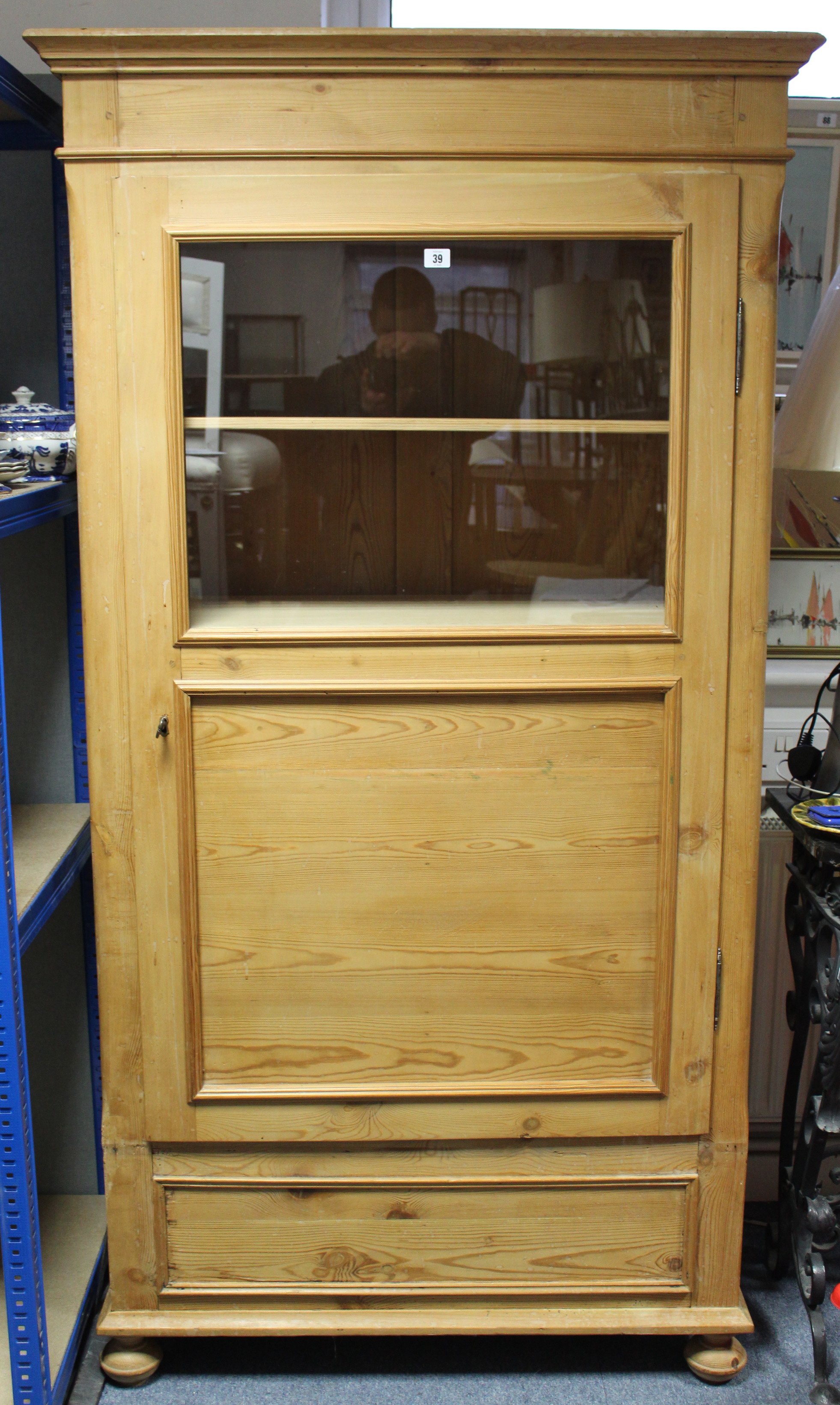 A continental-style tall pine cabinet fitted three shelves enclosed by glazed & panel door, & on bun