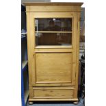 A continental-style tall pine cabinet fitted three shelves enclosed by glazed & panel door, & on bun