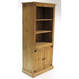 A pine tall standing bookcase with two open adjustable shelves above cupboard enclosed by pair of