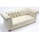 A Victorian three-seater buttoned chesterfield settee upholstered cream material, & on bun feet, 80”