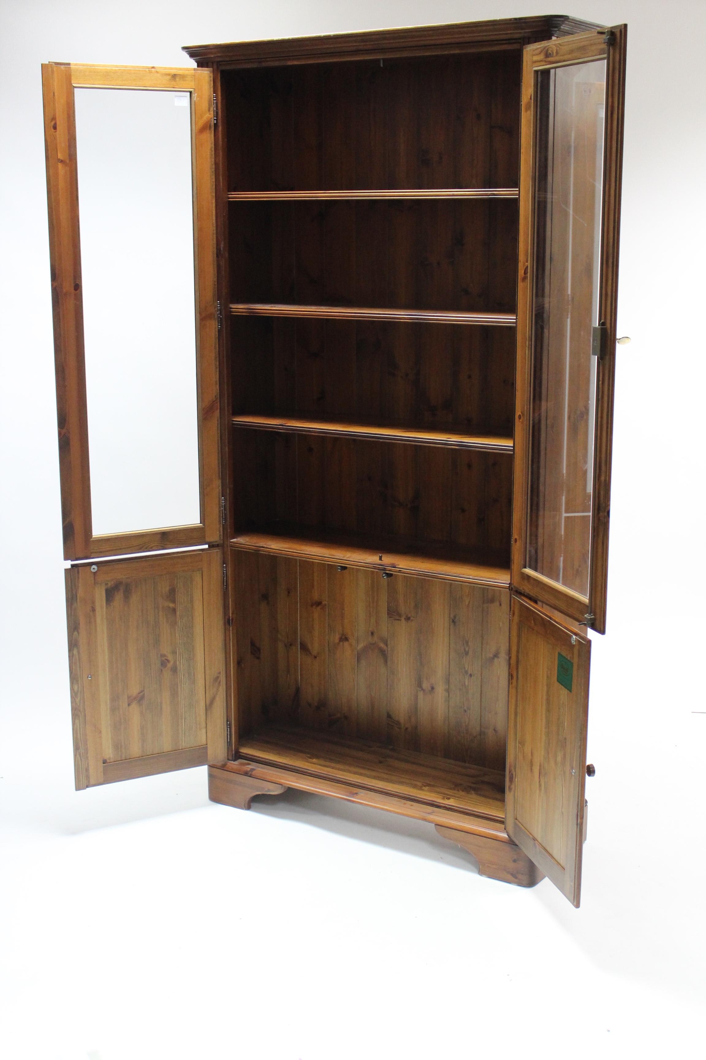 A Ducal pine tall cabinet, fitted five shelves enclosed by two pairs of doors, & on bracket feet, - Image 2 of 3