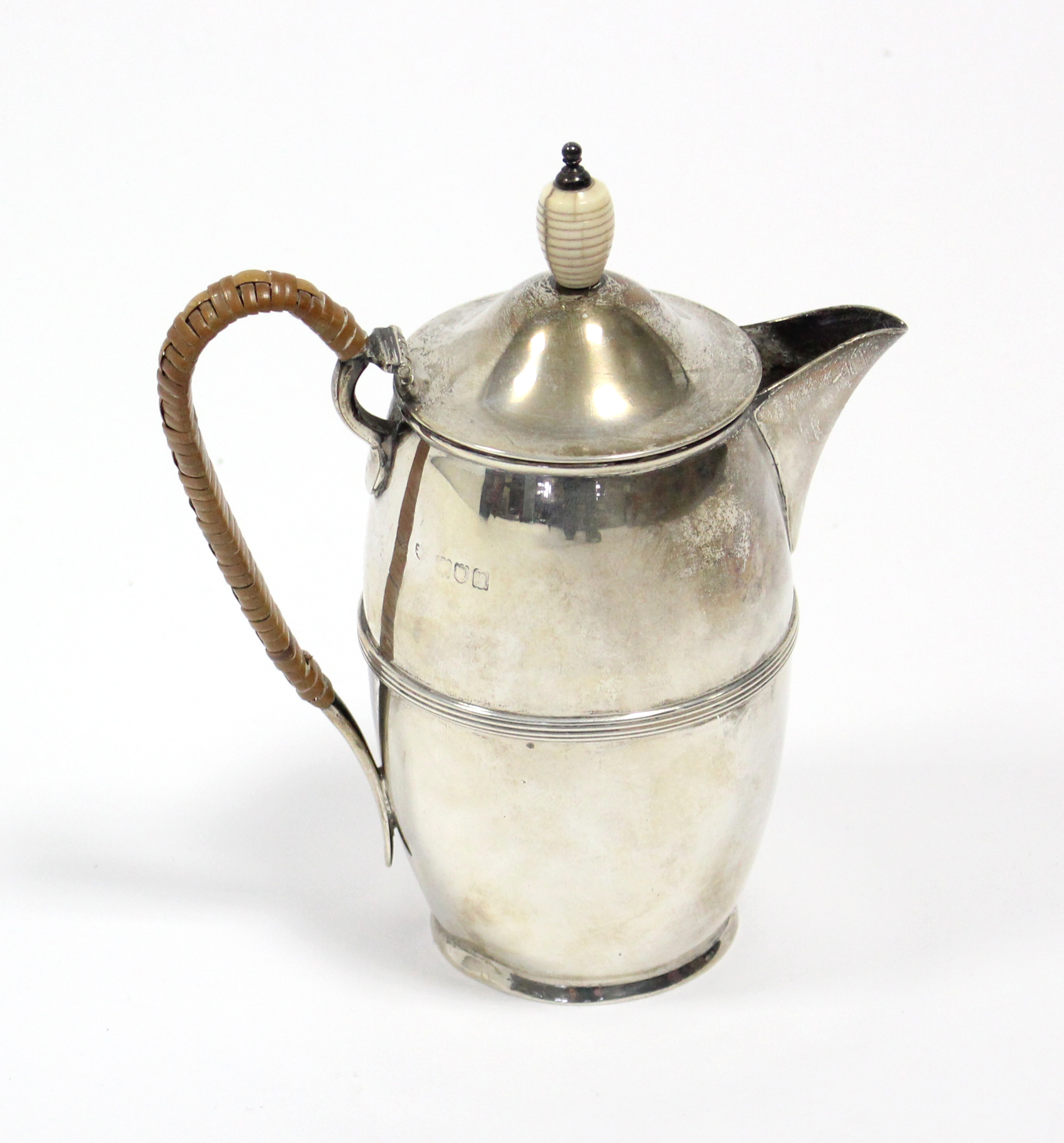 An Edwardian silver hot water jug of slender ovoid shape with reeded band around the girth, cane-