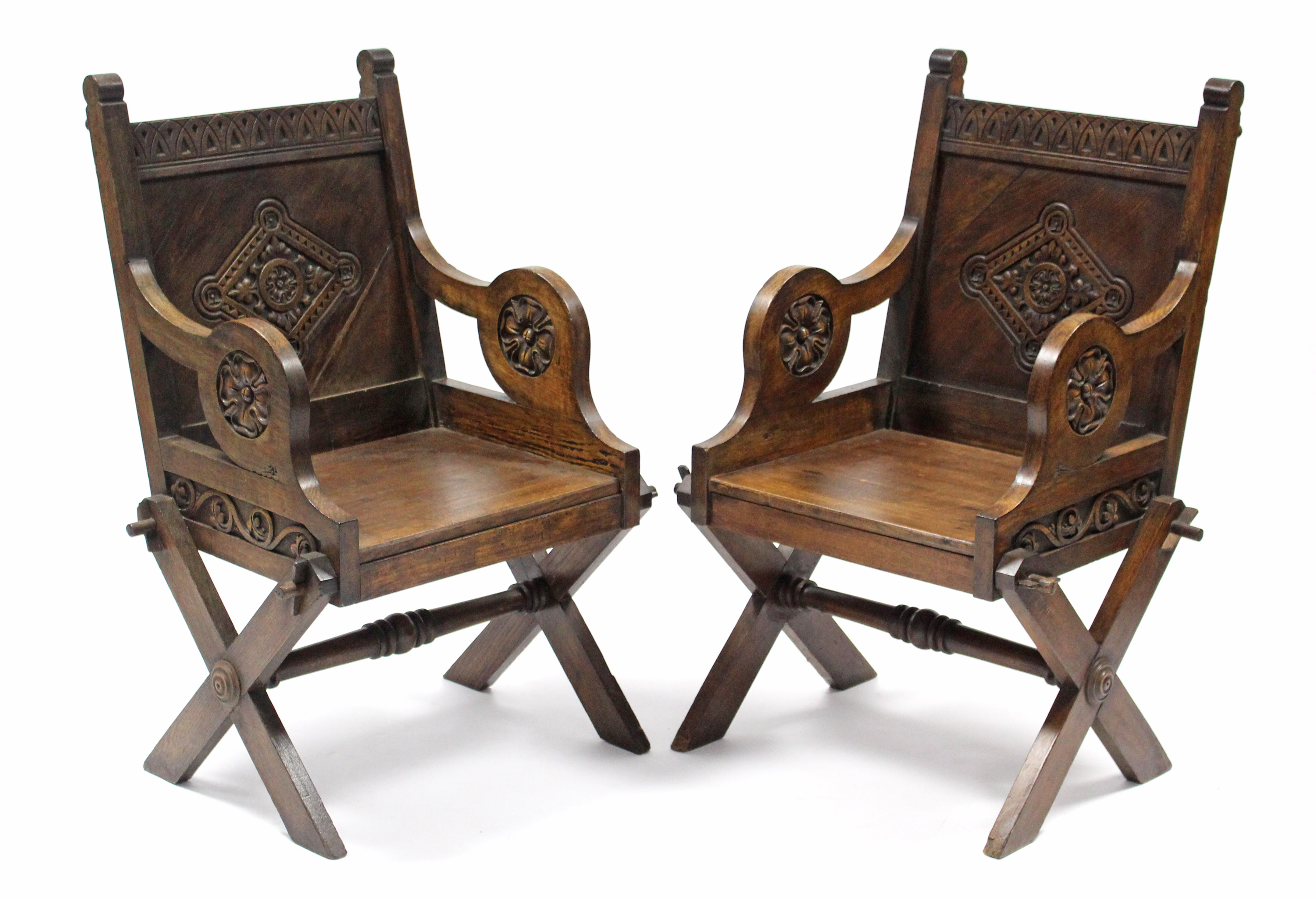 A pair of carved oak Glastonbury-type chairs with hard seats & scroll arms with Tudor Rose motif, on