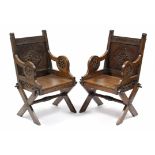 A pair of carved oak Glastonbury-type chairs with hard seats & scroll arms with Tudor Rose motif, on