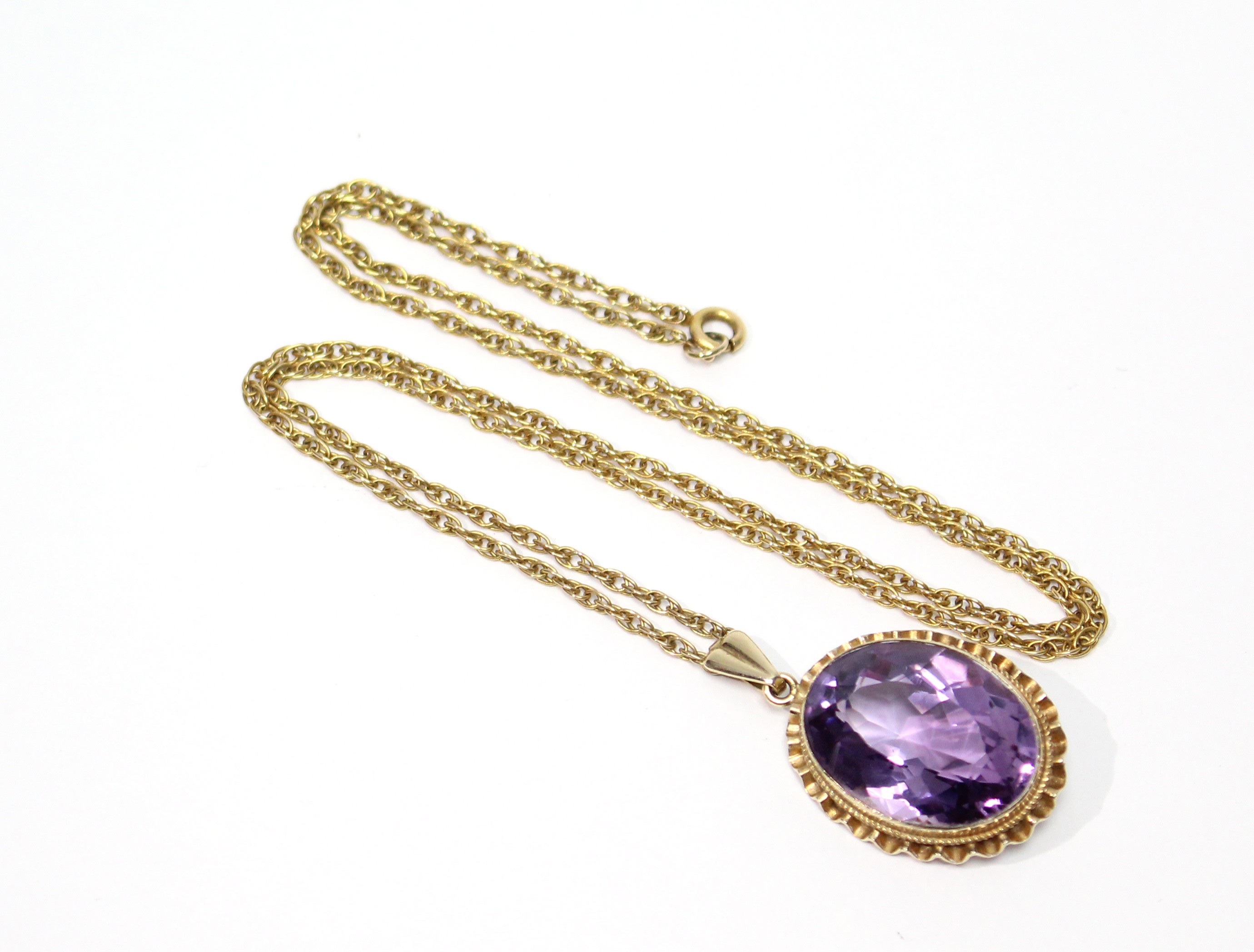 An oval-cut amethyst pendant in 9ct. gold mount, on yellow metal fine-link chain necklet.