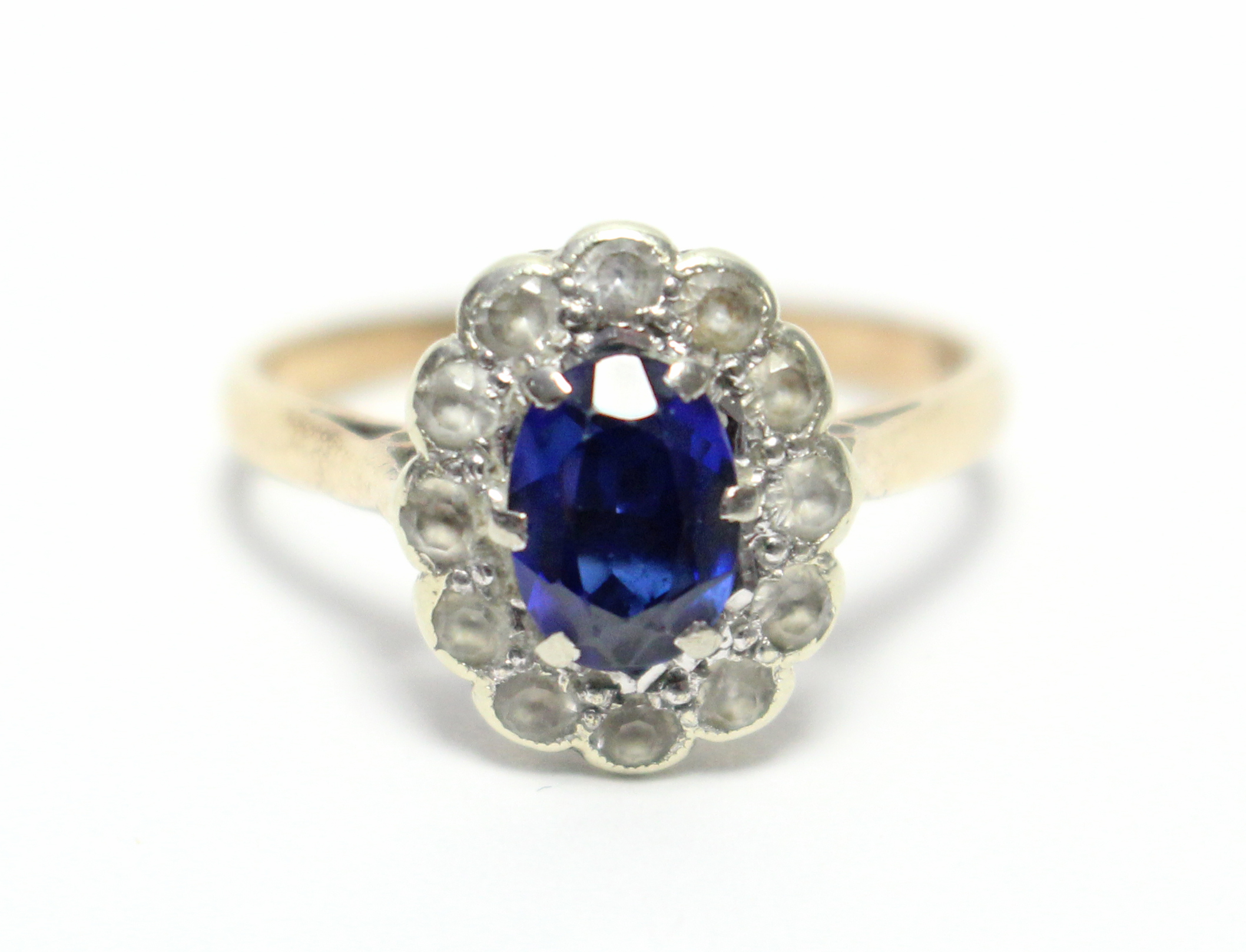 A 9ct. gold ring set oval synthetic sapphire within a border of small diamonds.