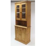 A pine tall cabinet, the upper part fitted two shelves enclosed by pair of glazed doors above an