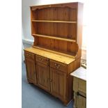A pine dresser, the upper part fitted two open shelves & with panelled back, the base fitted three
