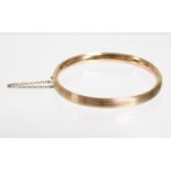 A 15ct. gold oval stiff hinged bangle with reeded exterior, & push clasp with safety chain. (10.