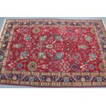 A Persian carpet of madder ground decorated with scattered stylised flowers within multiple borders,