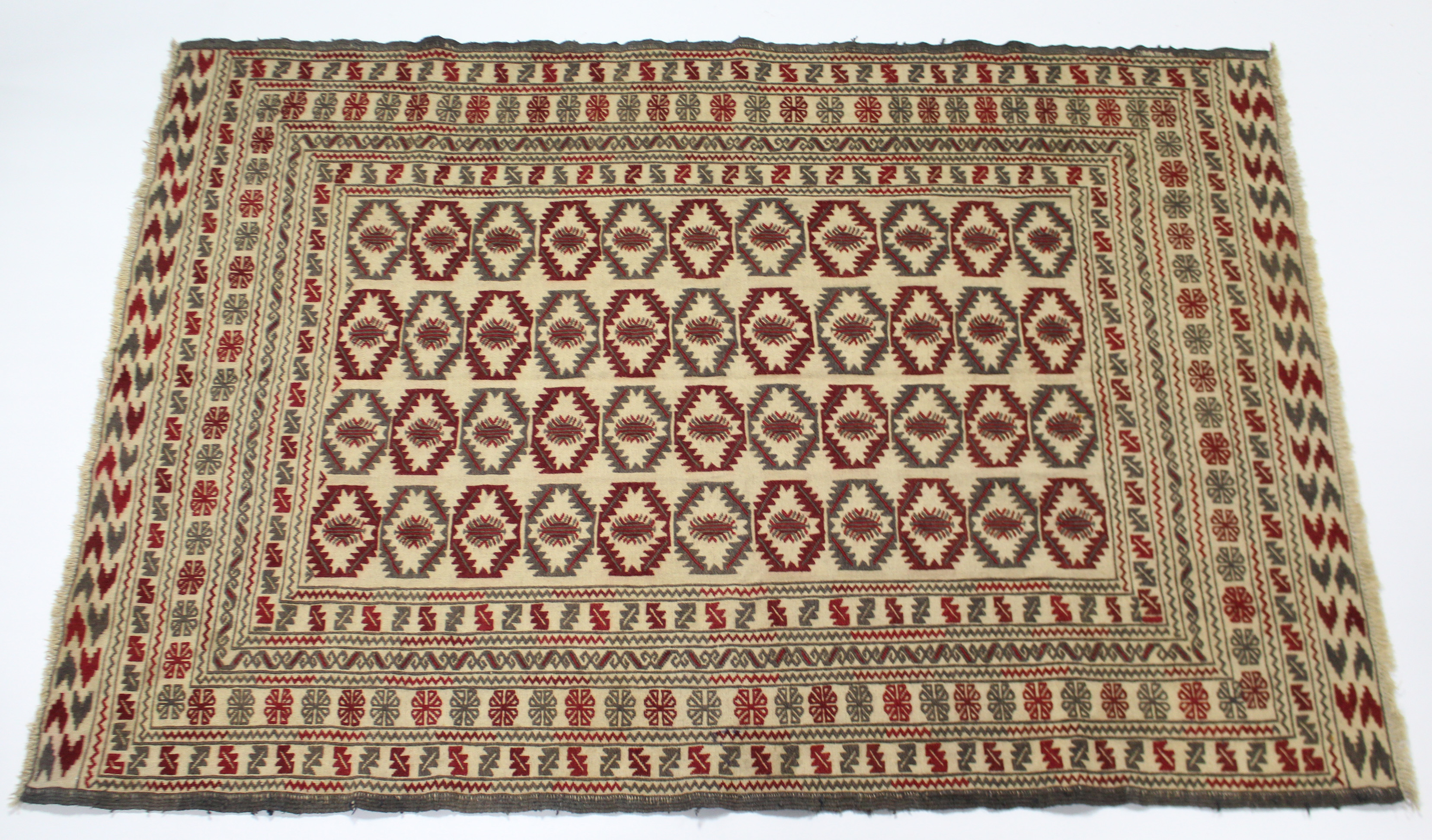 A needlework Sumac Kelim rug of ivory ground with central panel of lozenges within multiple