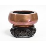 A Chinese heavy copper censer of plain squat oval shape, 5¼” wide x 2¼” high; on carved hardwood