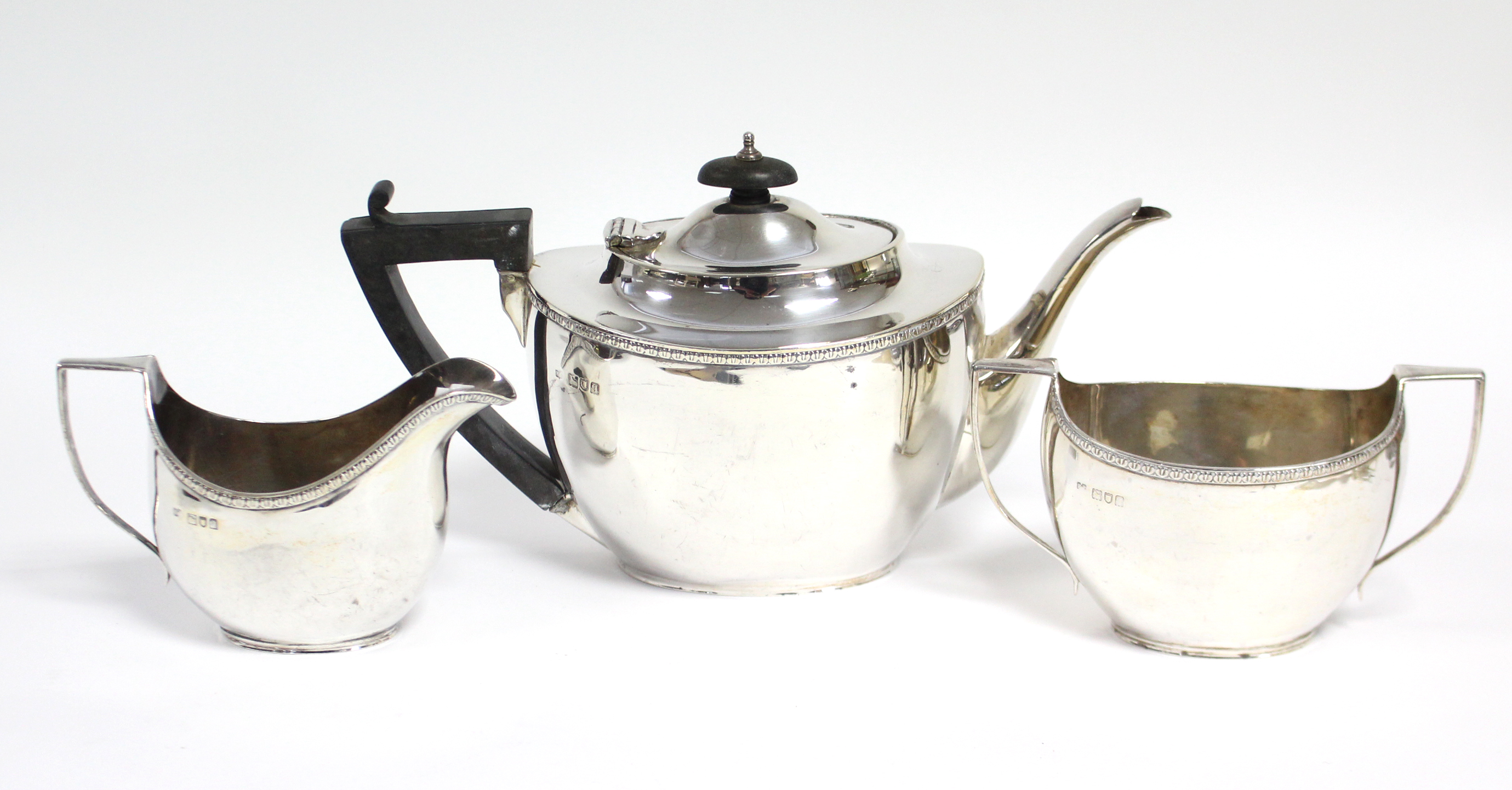 A George V silver three-piece tea service of plain oval form with narrow foliate rims; London