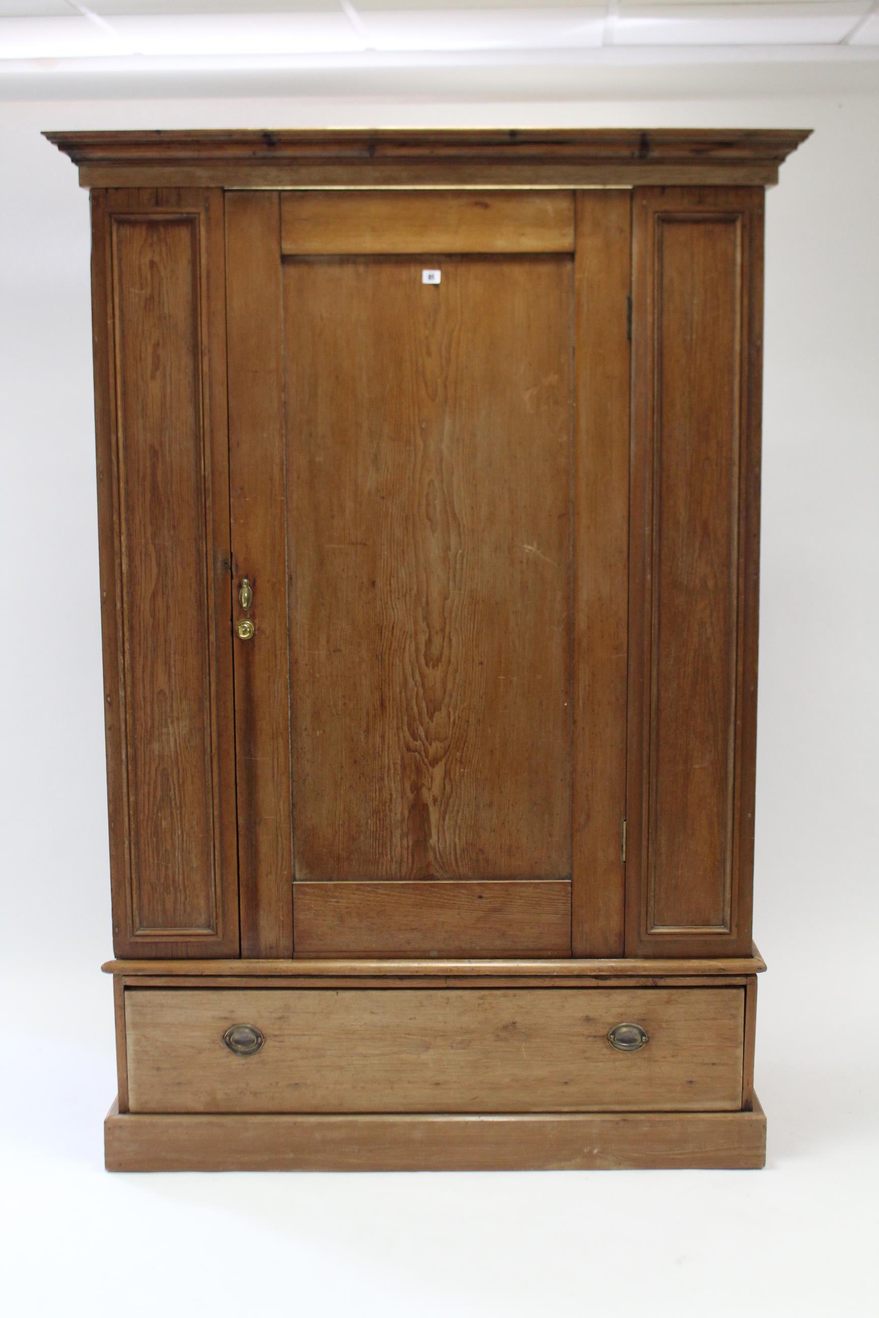 A pine wardrobe with moulded cornice, enclosed by centre panel door, & fitted deep long drawer to