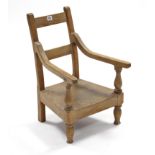 A light oak child’s rail-back elbow chair with hard seat & on turned legs.
