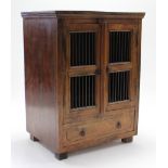 A hardwood upright cabinet, enclosed by pair of grille doors above a long drawer, & on block feet,