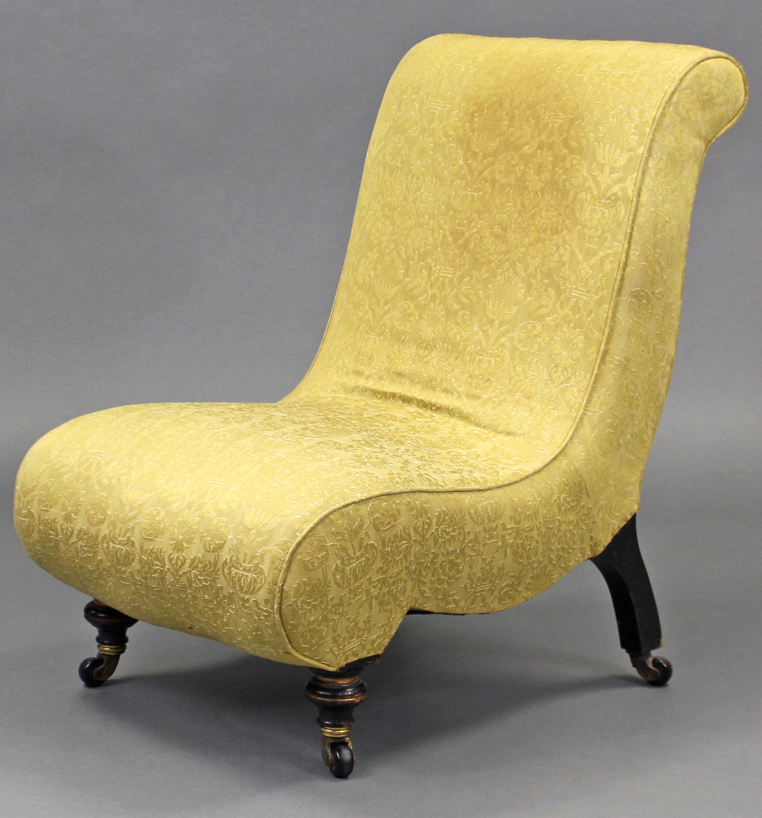 A Victorian nursing chair of scroll shape, upholstered yellow silk with repeating floral motif, on