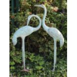 A pair of bronze life-size models of cranes, one with head raised, the other lowered, the feet