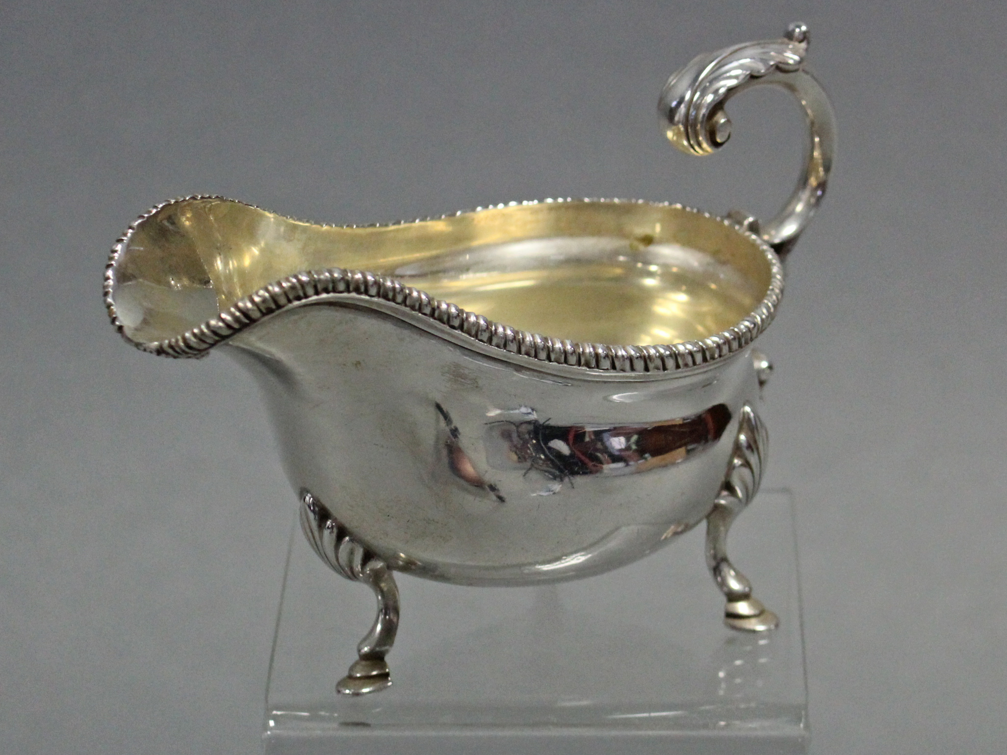 An Edwardian silver oval sauce boat with gadrooned rim, open acanthus scroll handle, & on three