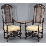 A pair of William & Mary style beech frame elbow chairs with carved scroll decoration, cane backs, &