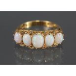 An 18ct. gold ring, scroll-set with five oval cut graduated opals, pairs of small rose diamonds in