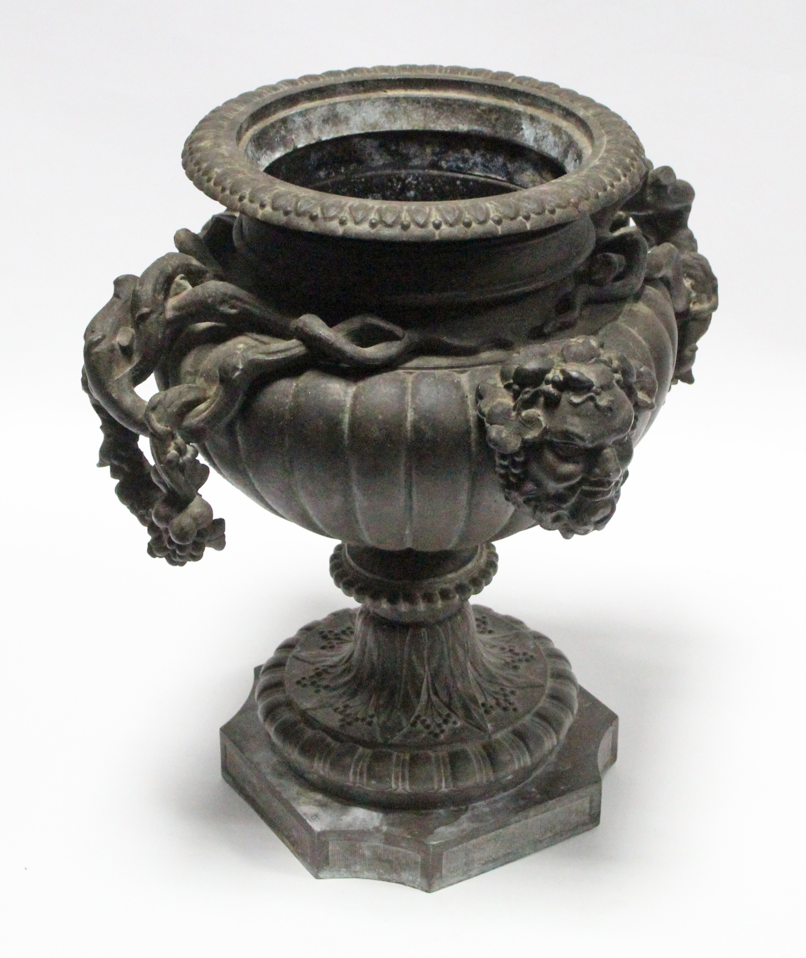 A 19th century bronze urn of fluted ovoid form, with grapevine side handles & Bacchus masks, on