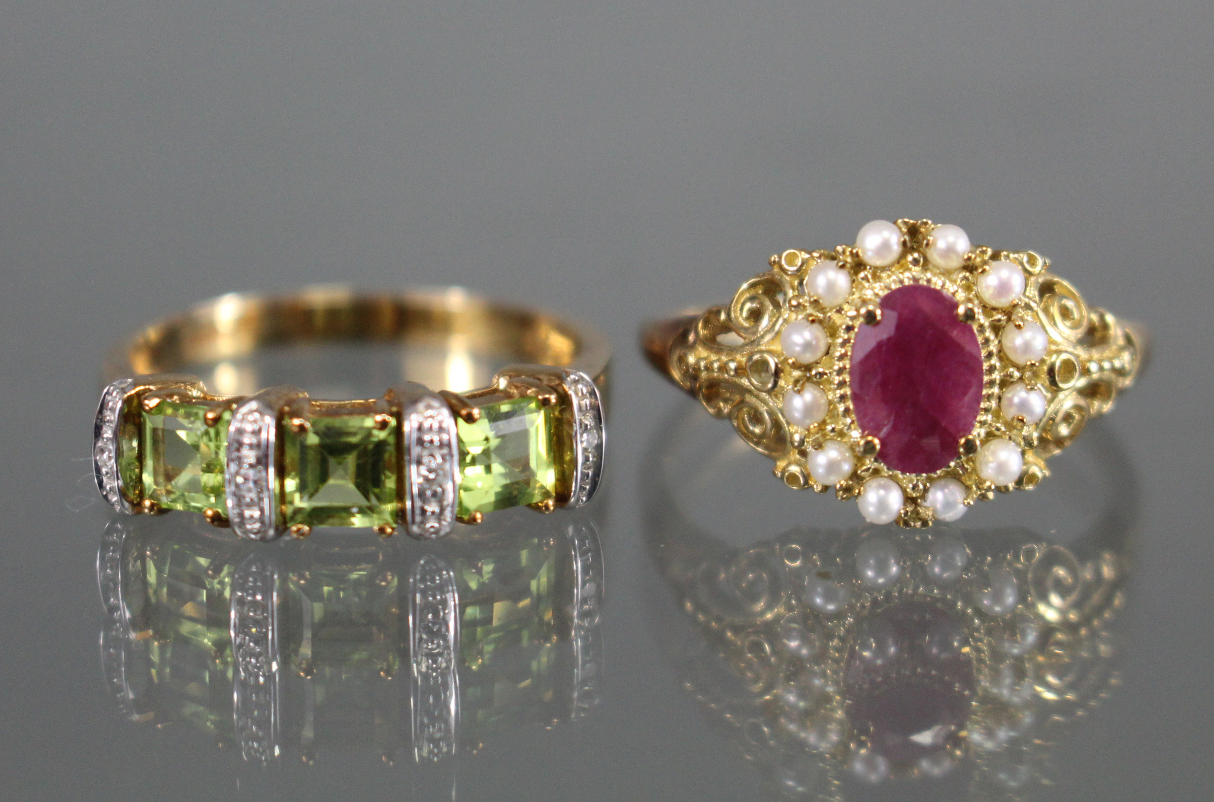 An un-marked yellow metal ring set oval ruby within a border of seed pearls & with pierced scroll