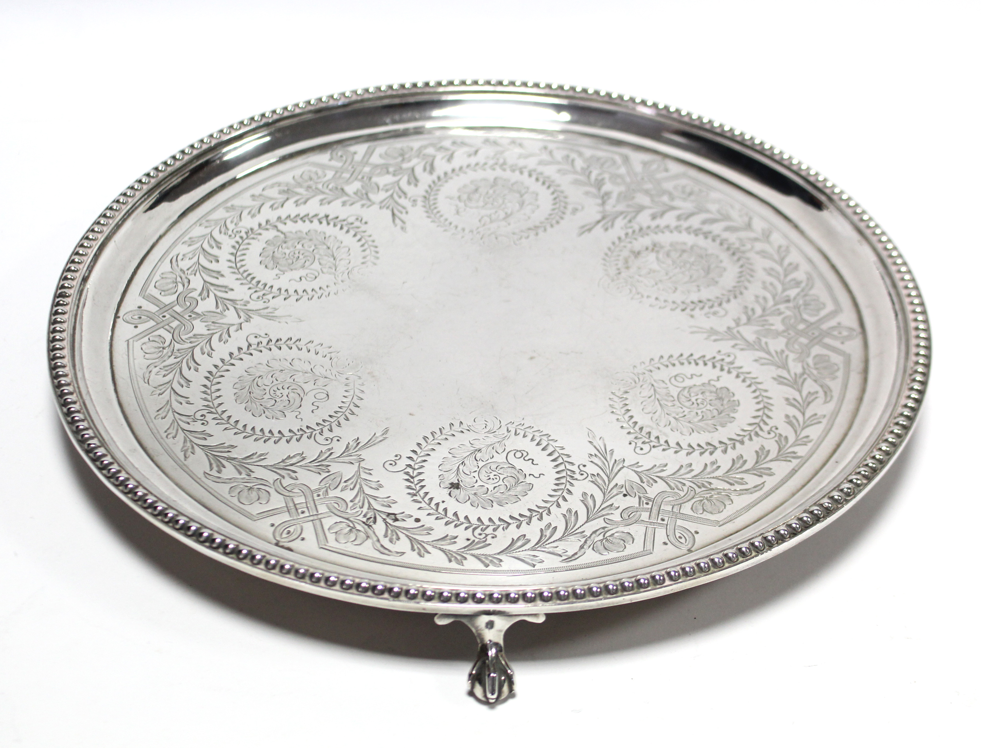 A Victorian silver waiter with engraved leaf-scroll decoration within a beaded rim, on three