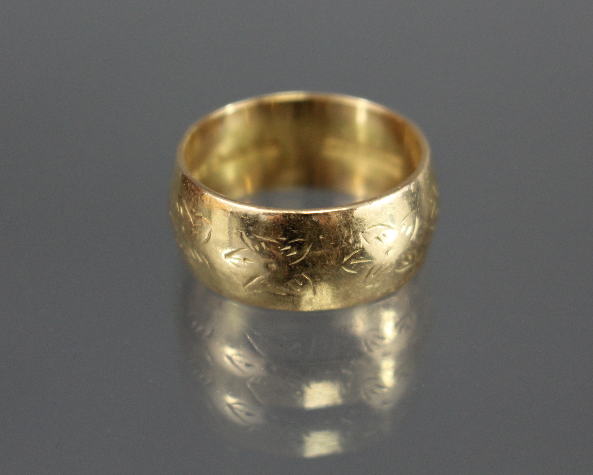 An 18ct. gold wedding band with engraved flower-head design; Birmingham hallmarks for 1991. (Size: