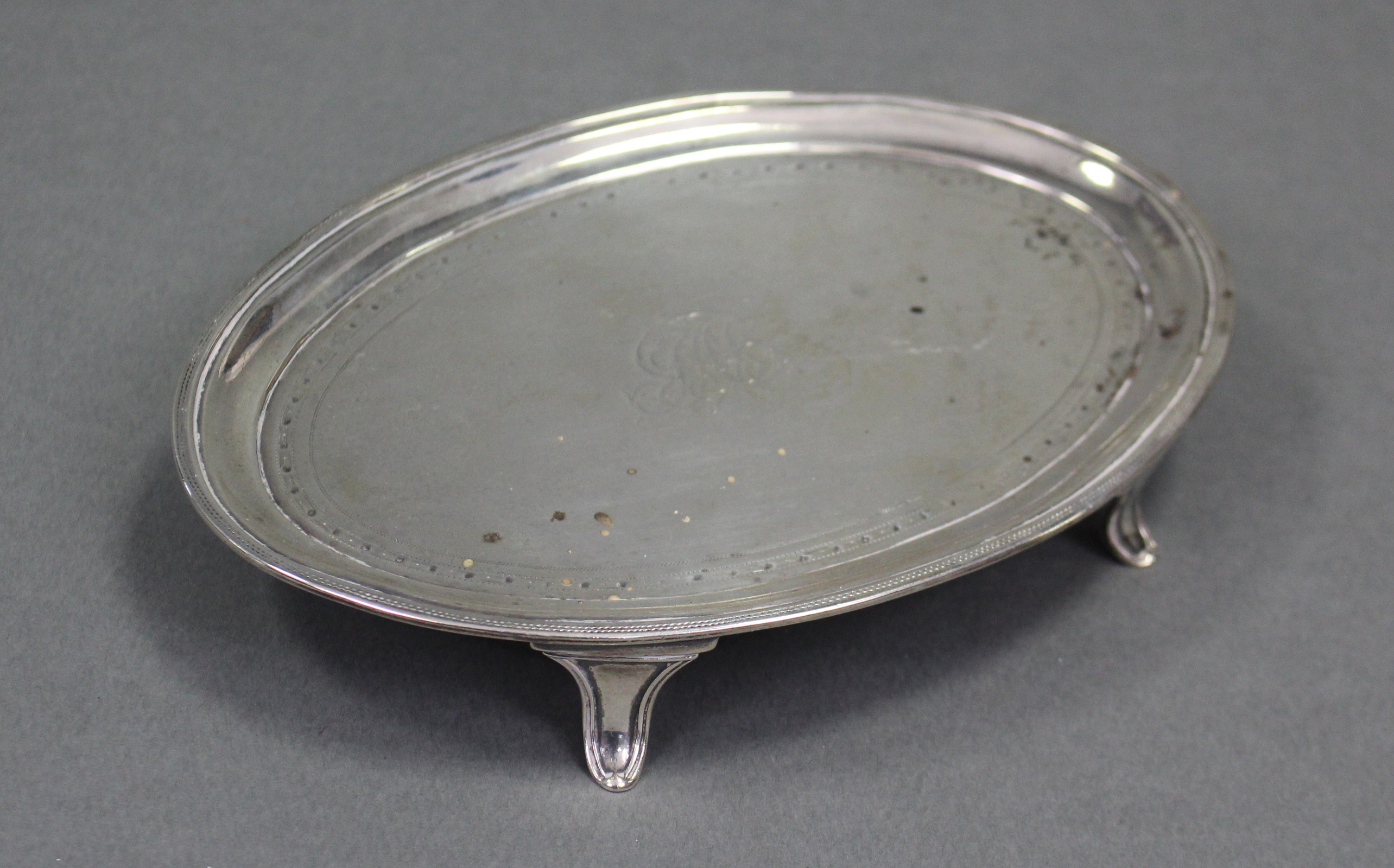 A George III silver oval teapot stand with pricked borders, engraved monogram to centre, & on four