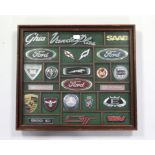 A framed display of various car emblems & badges including Porsche, Jaguar, Lancia, etc. together