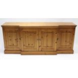 A pine break-front low sideboard enclosed by two pairs of panel doors, & on plinth base, 74” long