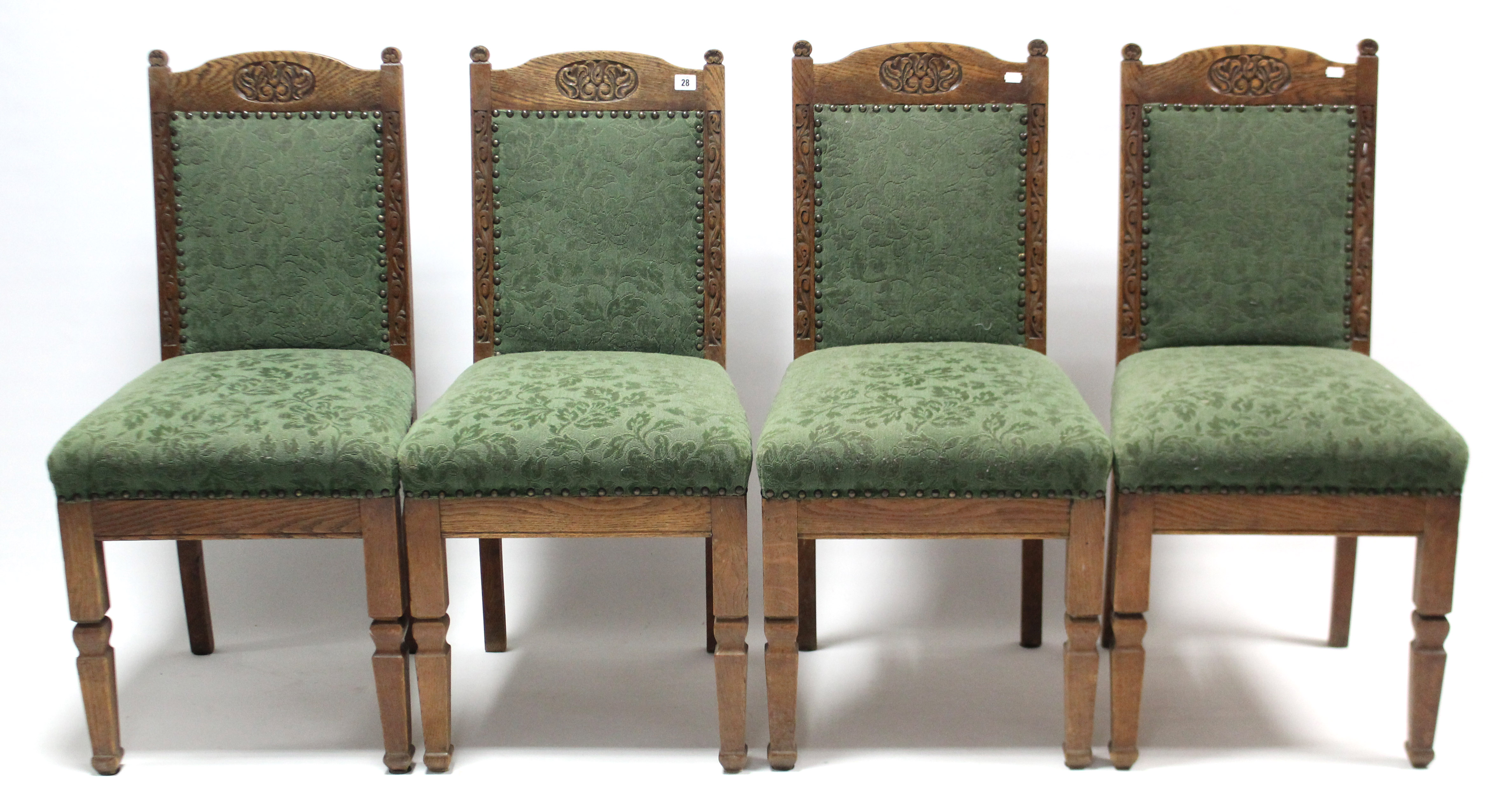 A set of four Edwardian carved oak rail-back dining chairs with padded backs & sprung seats, & on