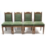 A set of four Edwardian carved oak rail-back dining chairs with padded backs & sprung seats, & on