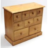 A small pine chest, fitted with an arrangement of nine drawers with turned knob handles, & on plinth