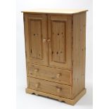 A pine upright cupboard, enclosed by pair of fielded panel doors above two long drawers, & on shaped