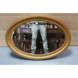 A gilt frame oval wall mirror with egg-&-dart border, & inset bevelled plate, 25” x 34¾”.