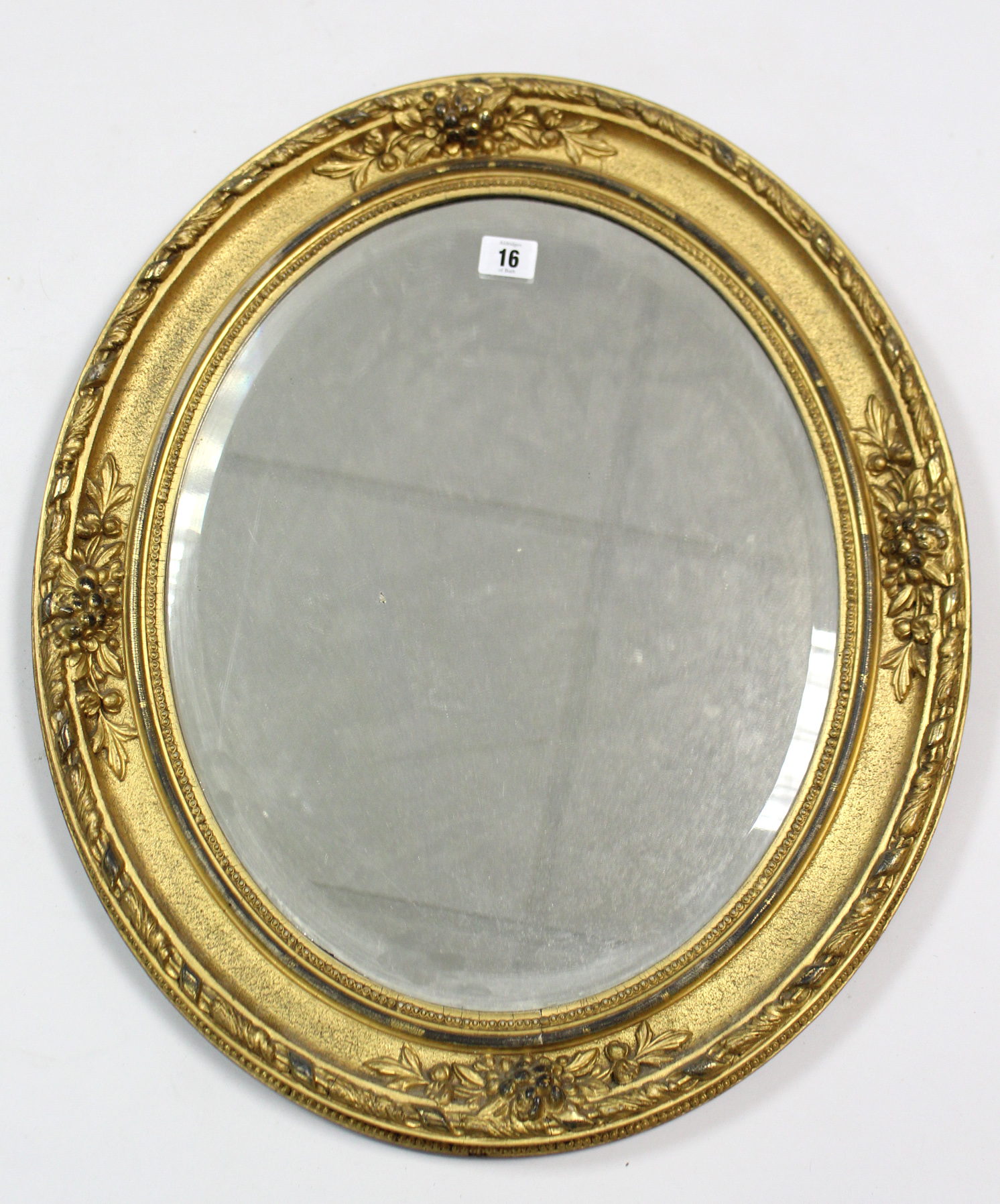 A gilt-frame oval wall mirror with raised foliate border & inset bevelled plate, 23” x 19½”.