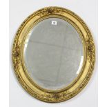 A gilt-frame oval wall mirror with raised foliate border & inset bevelled plate, 23” x 19½”.