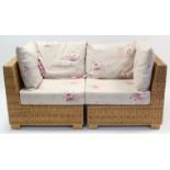 A rattan two-seater settee with floral-printed loose cushions, 62” long.