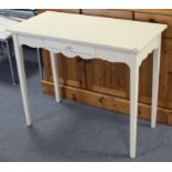A white-finish side table fitted centre frieze drawer, & on square tapered legs, 36” wide.