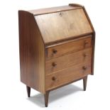 A teak bureau with fitted interior enclosed by fall-front above three long graduated drawers, & on
