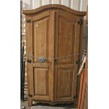 A continental-style pine wardrobe with rounded top, & enclosed by pair of fielded panel doors,