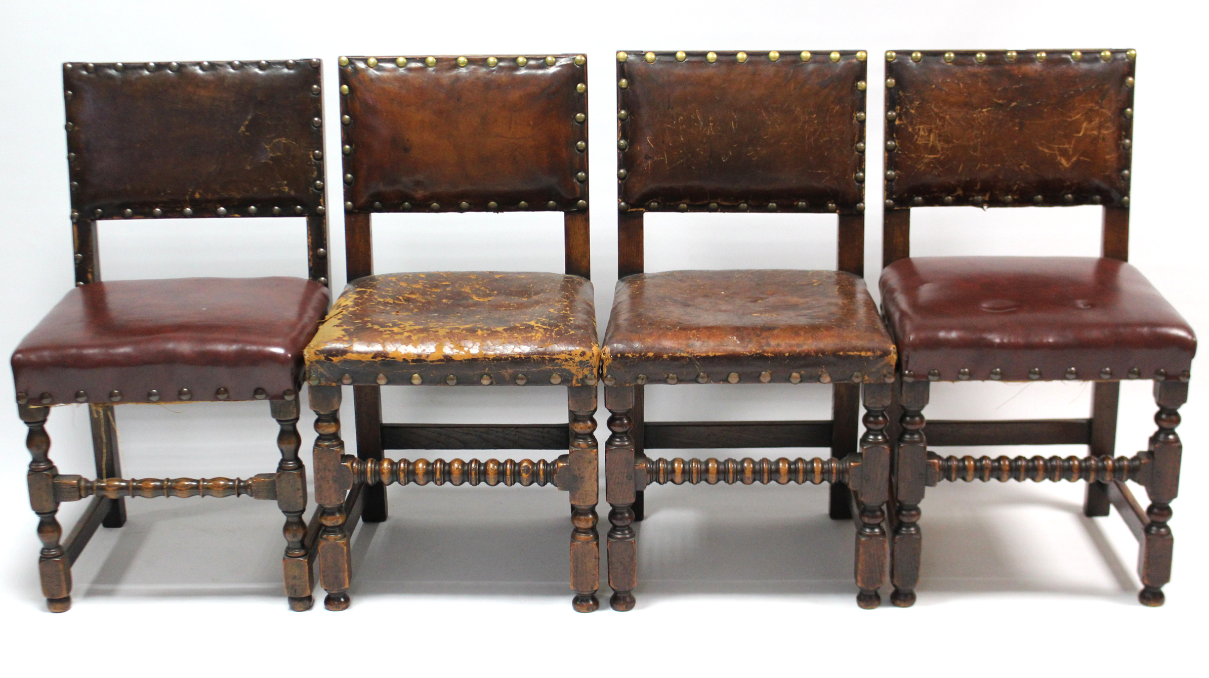 A set of four Cromwellian-style oak dining chairs with brass studded seats & backs, & on turned legs
